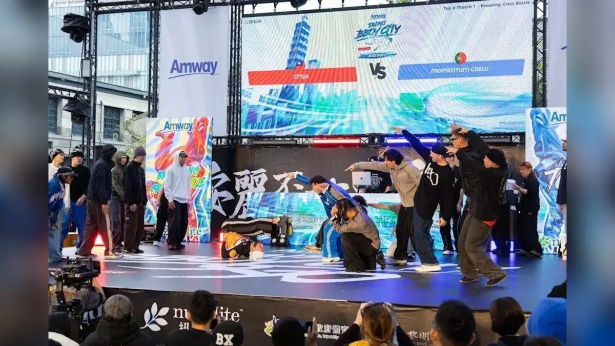 高雄室內賽場上，一名亞洲舞者做出定格動作，隊友在後方圍成半圈應援。