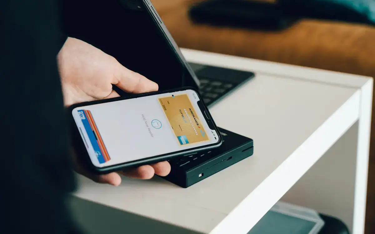 手機靠近感應式付款終端機，畫面以抽象化代號呈現信用卡 Apple Pay 的 Token 化流程（示意圖）