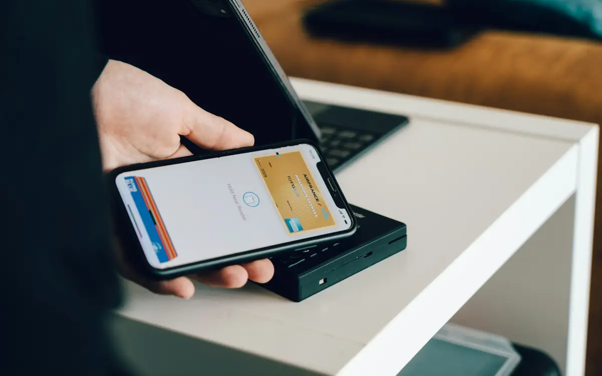 手機靠近感應式付款終端機，畫面以抽象化代號呈現信用卡 Apple Pay 的 Token 化流程（示意圖）