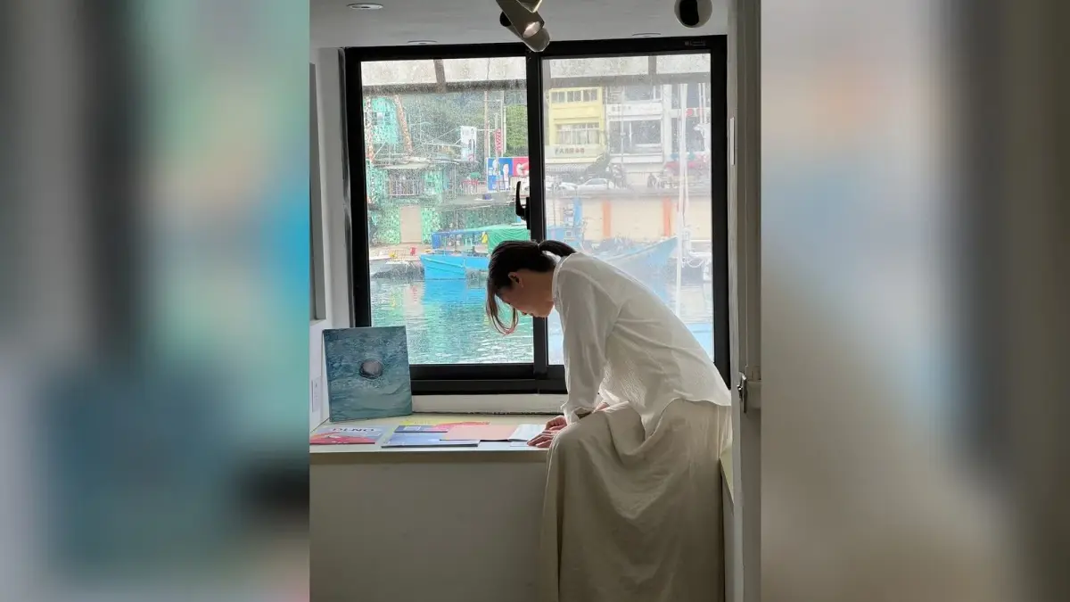 窗邊可見正濱漁港水面與船隻，吳丹文在室內展場俯身整理桌上的作品資料。