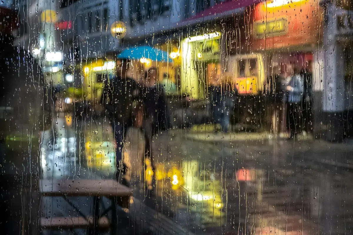 雨滴落在窗面，窗外城市景色因雨勢而模糊。