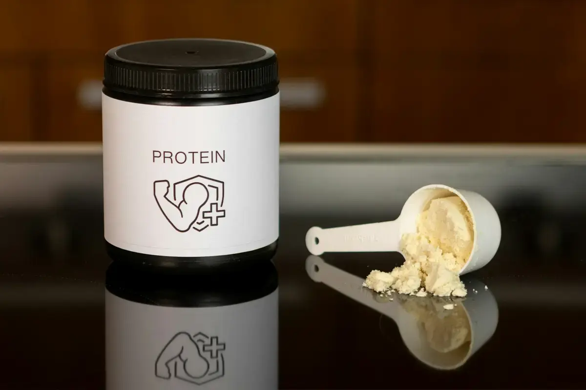 乳清蛋白粉罐、白色量匙、搖搖杯與牛奶放在桌面上