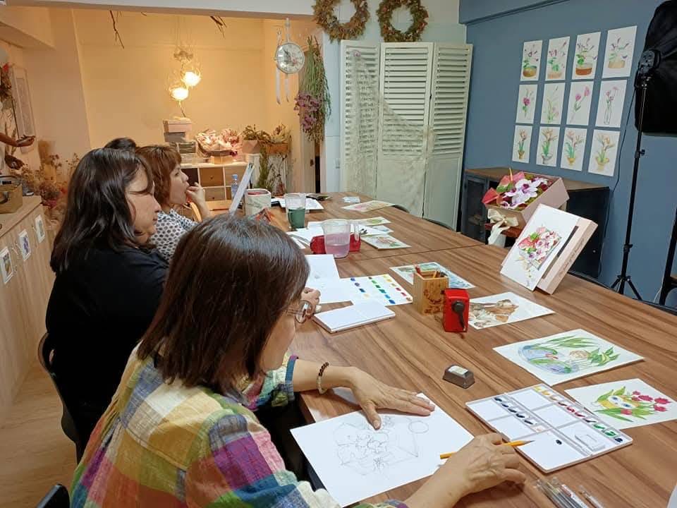 成人學員在畫室練習水彩,桌面上有畫紙、色票與多幅花卉作品