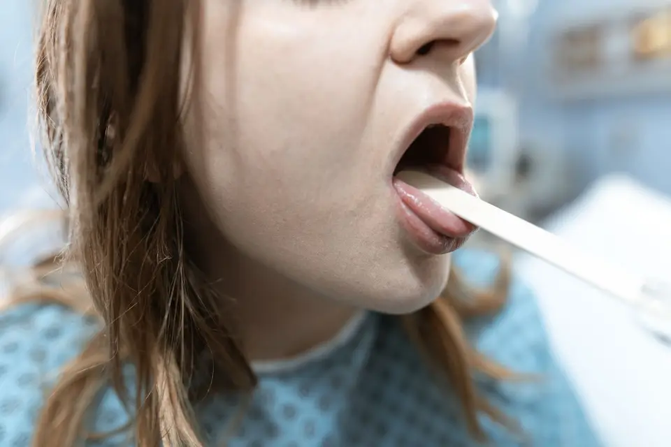 有發燒、咳嗽、喉嚨痛等呼吸道症狀應儘速就醫檢查(示意圖) 醫生用壓舌板檢查患者的喉嚨。