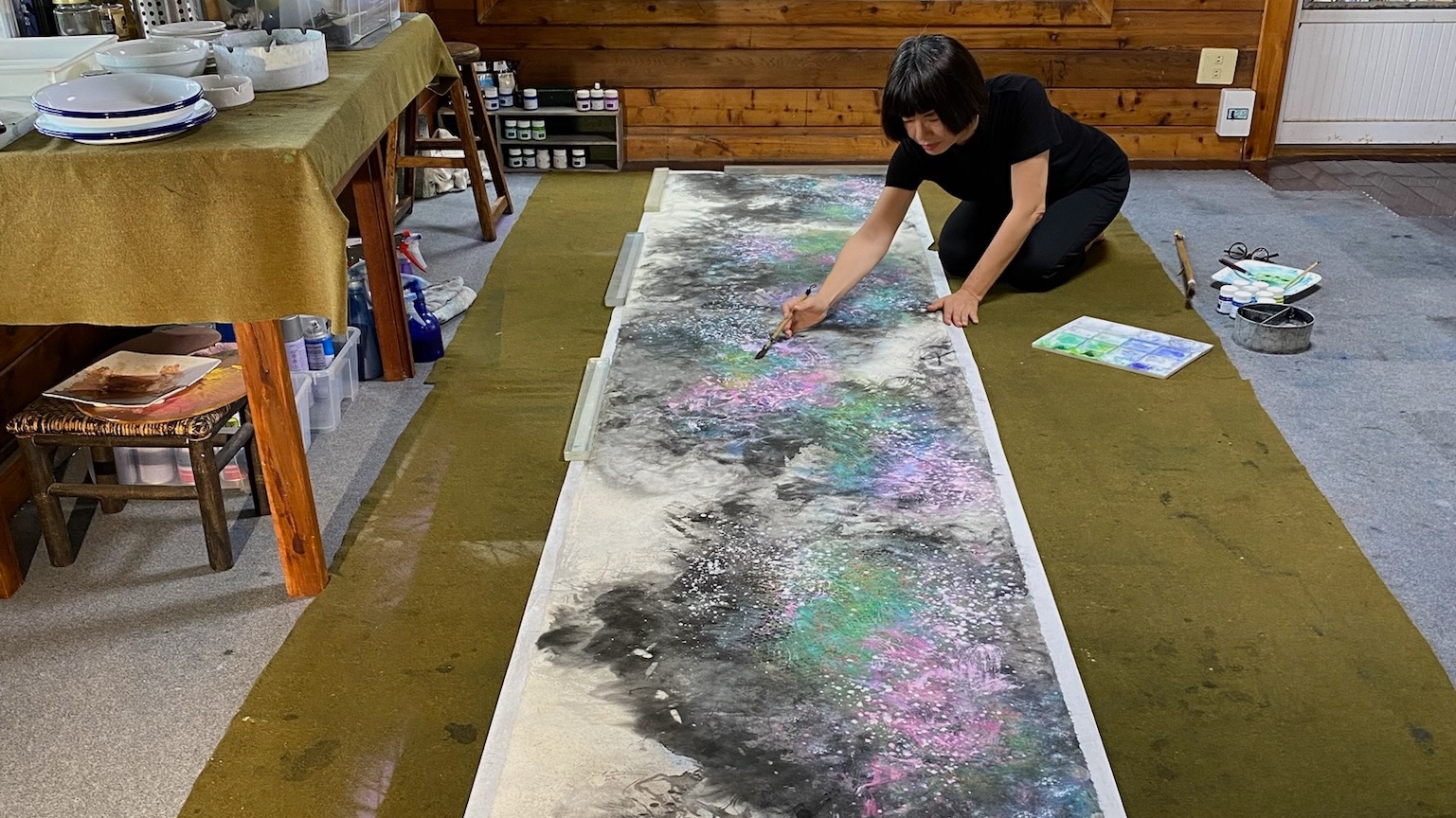 江心靜在工作室中俯身描繪長幅作品