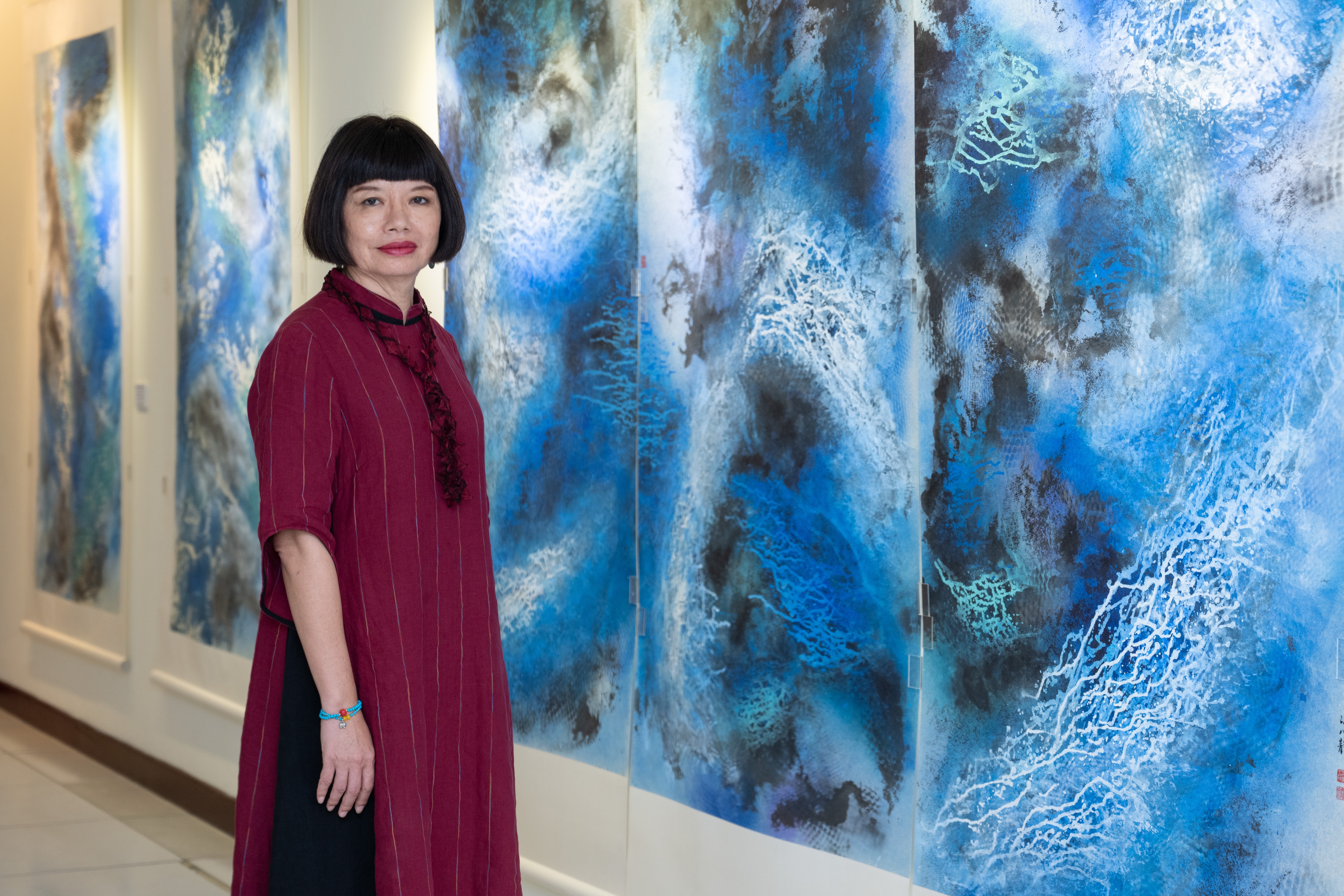 江心靜與同行者在展覽作品前合影,畫作以藍白色調描繪流動感