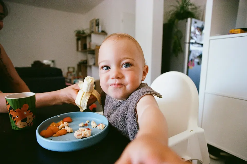 幼童坐在椅子上，成人的手在旁邊輔助餵食