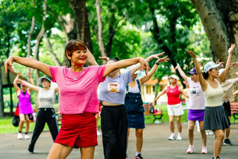 一群中高齡女性在公園戶外空間跟著帶領者做伸展體操,面帶微笑、精神飽滿
