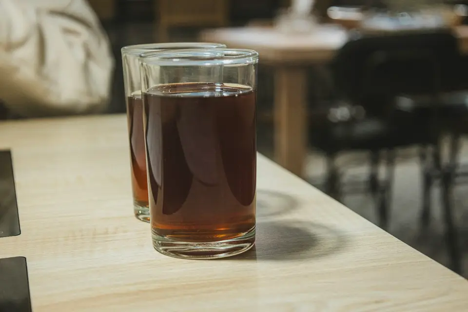 將冰紅茶從調飲器倒入玻璃杯的飲料桌面場景，呈現泡沫紅茶的飲用方式