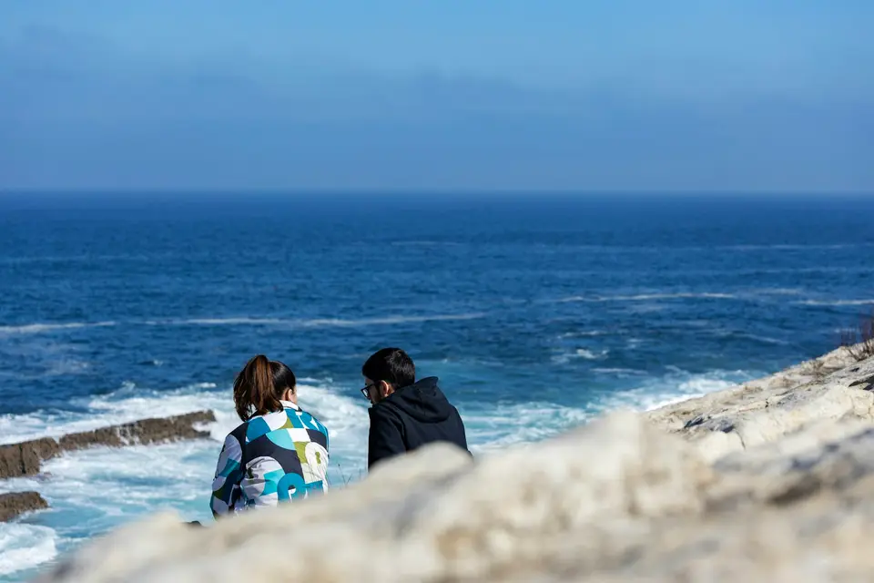 兩名旅客坐在花蓮海岸旁眺望海面
