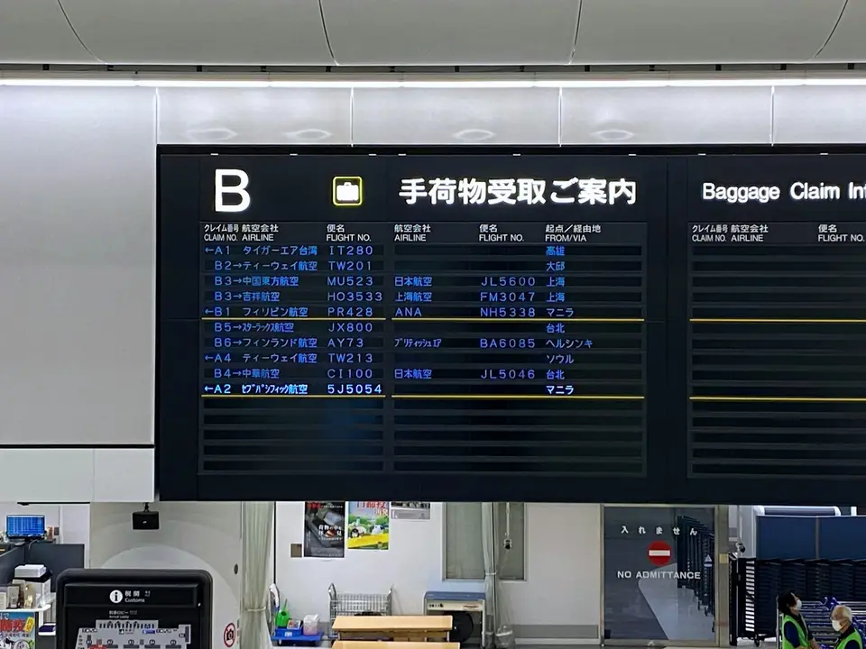 機場行李提領區的航班資訊看板與行李服務設備，呈現旅客抵達日本後依指示前進的情境