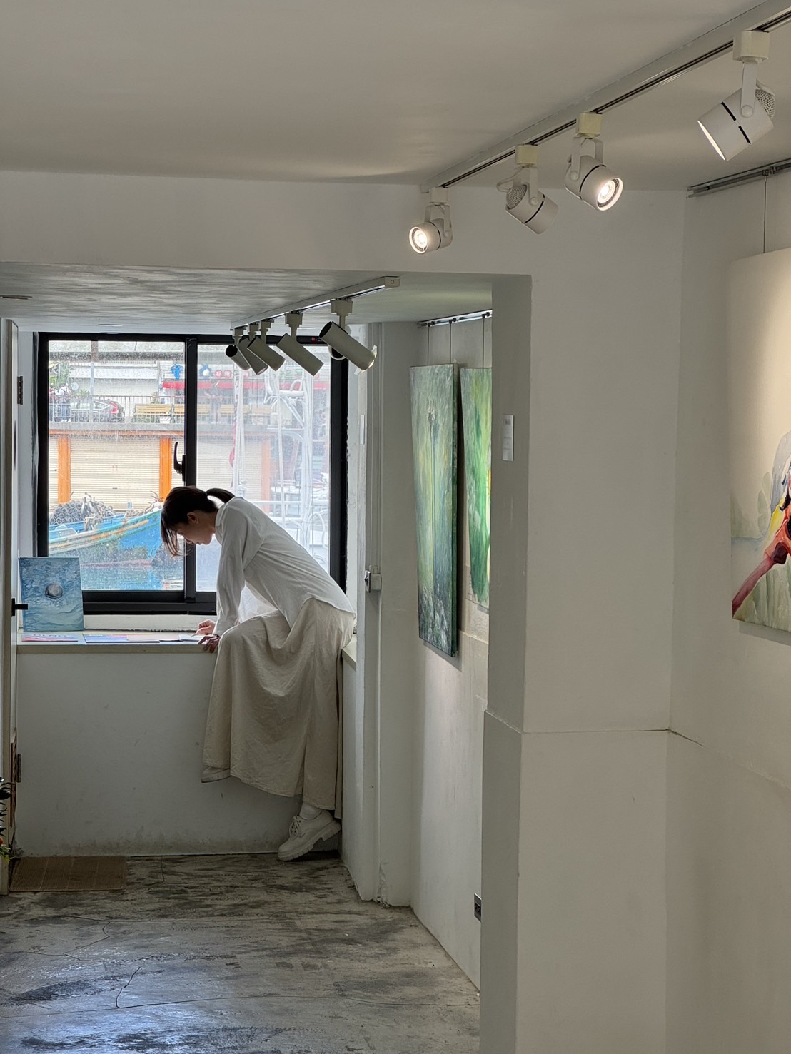 吳丹文在 SPACE MOOR 窗邊工作，狹長展間與港口景色同時入鏡。
