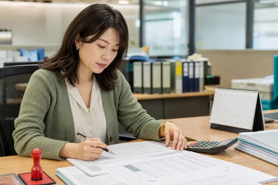辦公桌上有人核對付款文件與計算機，呈現由給付單位代扣補充保費的情境