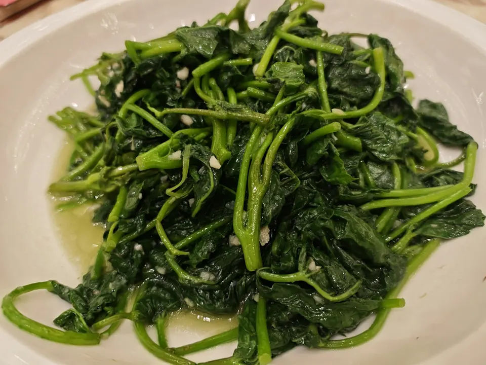 白色圓盤中盛放一大盤翠綠色炒菠菜，菠菜已炒軟帶有少許蒜末，色澤鮮亮