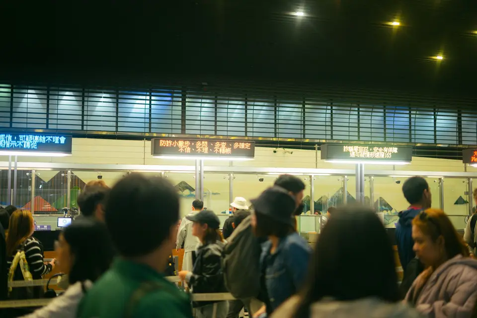 機場報到櫃檯前的旅客與航班資訊，呈現等待航班公告與售票的情境