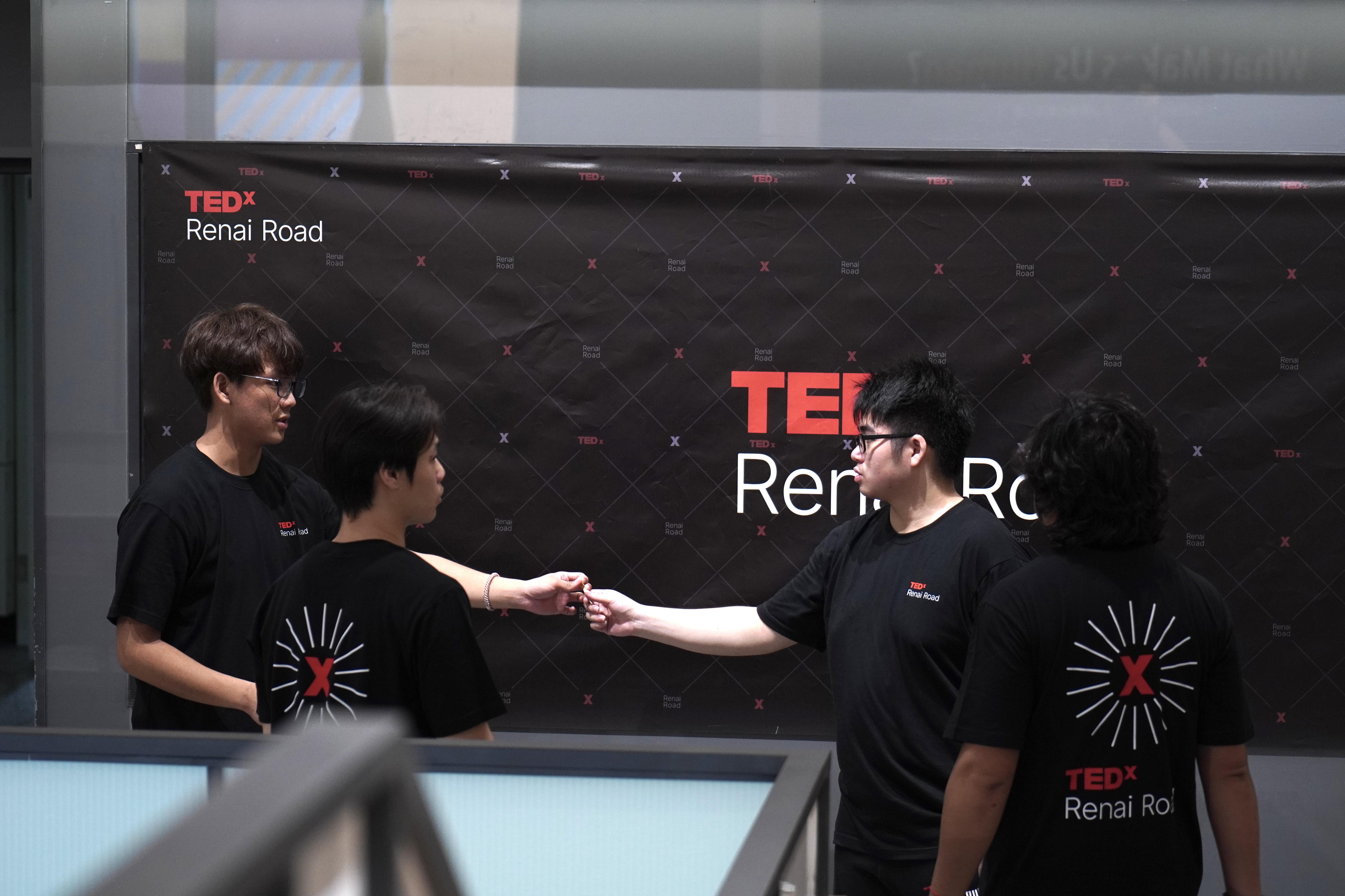 TEDxRenaiRoad志工在活動海報前進行工作交接,呈現現場協作與任務銜接