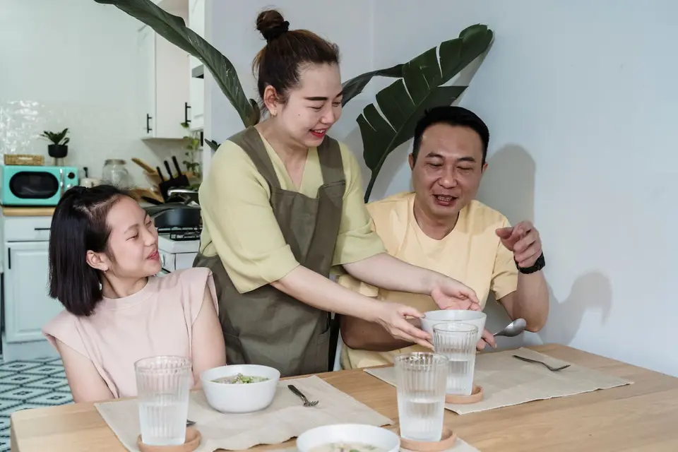 家庭餐桌旁的大人準備食物,呈現陪伴孩子用餐與家長示範的情境