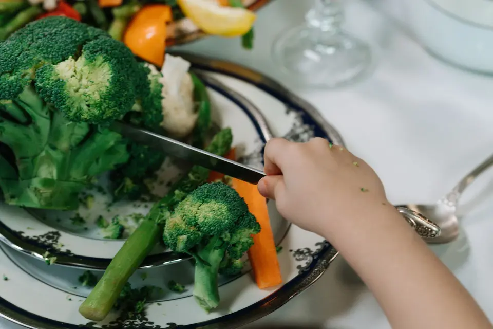 幼兒餐盤放著花椰菜與其他蔬菜,旁邊有手部準備食物