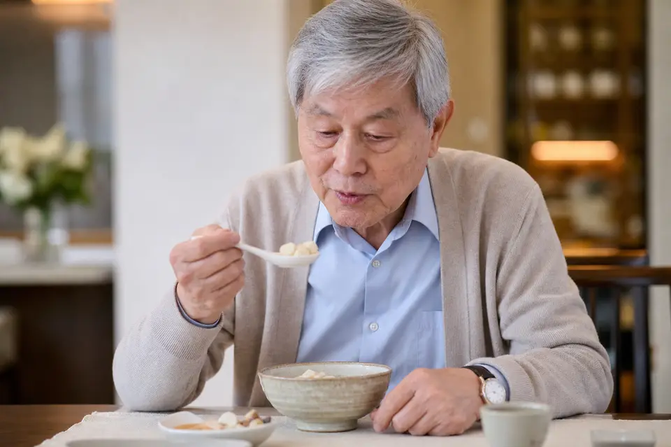 長者以湯匙小口進食湯圓,桌上放著溫熱餐碗,呈現吞嚥安全提醒