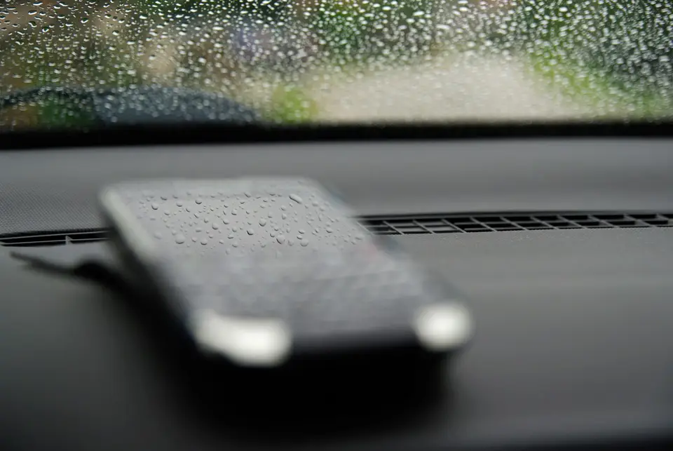 雨天窗邊桌面上的手機顯示政府災害公告頁面，旁邊有雨滴與防災資料