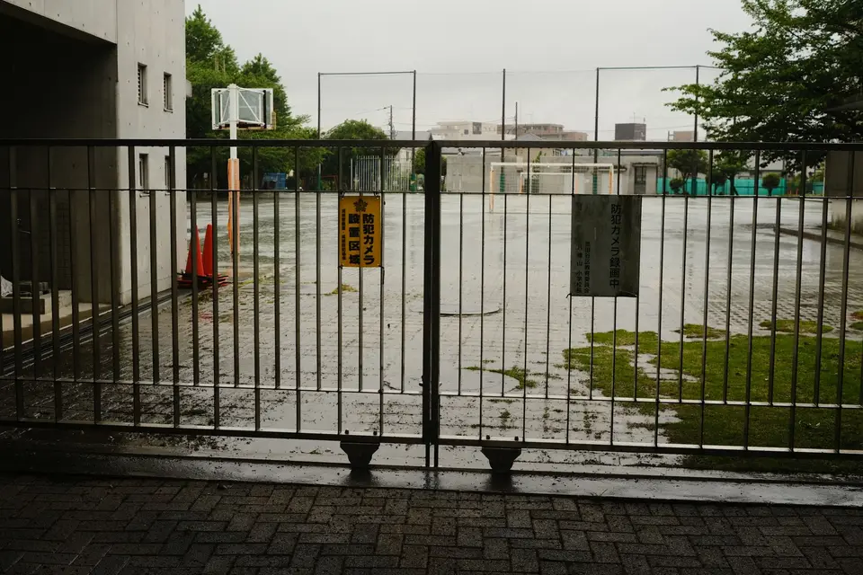 雨天校園入口的公告欄與校舍，公告欄上有防災通知紙張但沒有可辨識私人資料