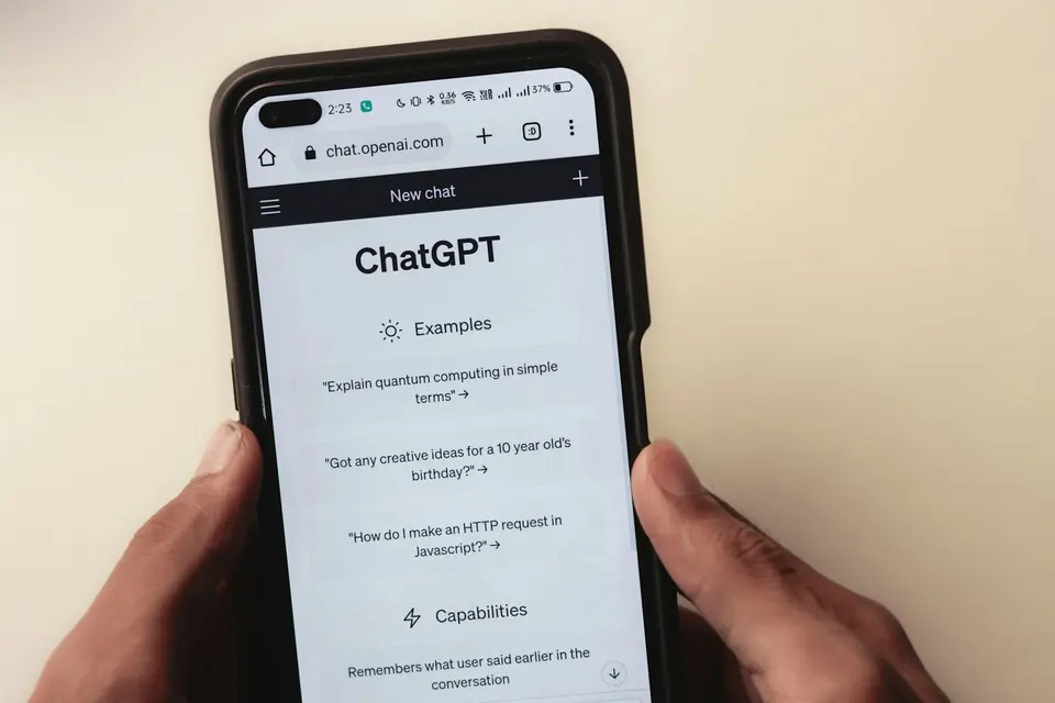 雙手握著顯示 ChatGPT 介面的手機,螢幕上可見對話輸入框與示例提示