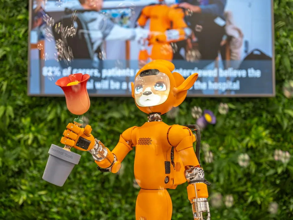 橘色人形醫療機器人站在展示牌前,牌上顯示醫療 AI 相關統計數字,背景為植物牆